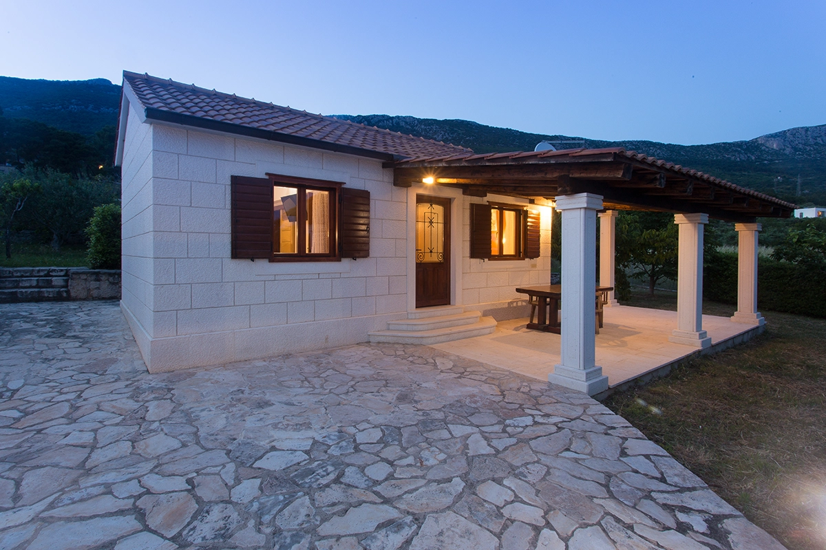 View of the front side of the illuminated villa at dusk, a stone villa with an entrance area.